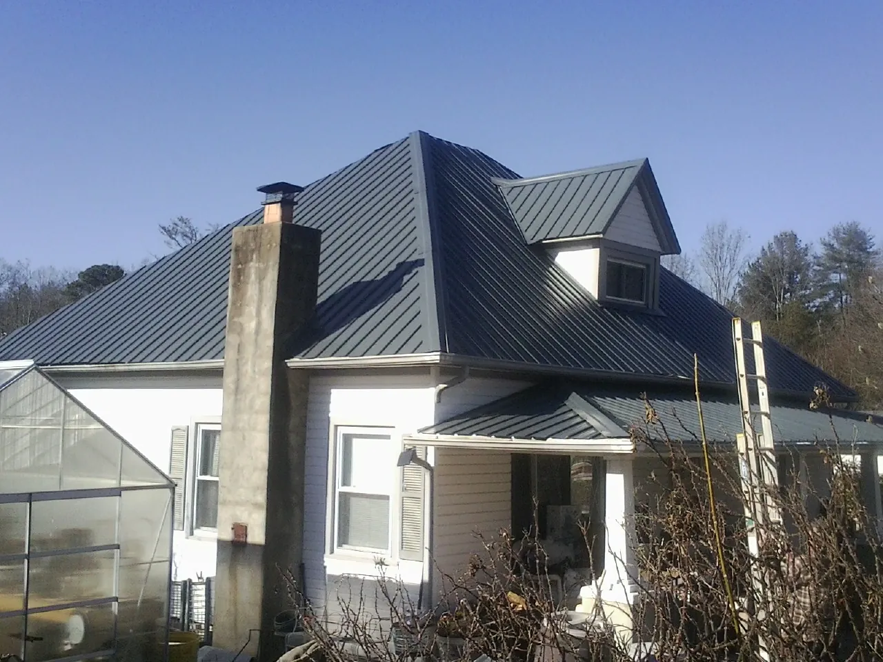 Dark blue standing seam metal roof on a white farmhouse with dormer — Slate & Tile Roof Repair by Roofing Brothers in Trumansburg