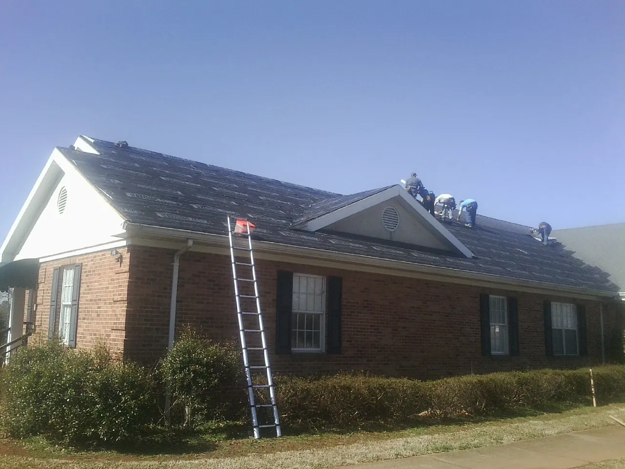Crew tearing shingles off a brick ranch roof with a ladder set — Emergency Roof Repair work by our crew in Trumansburg