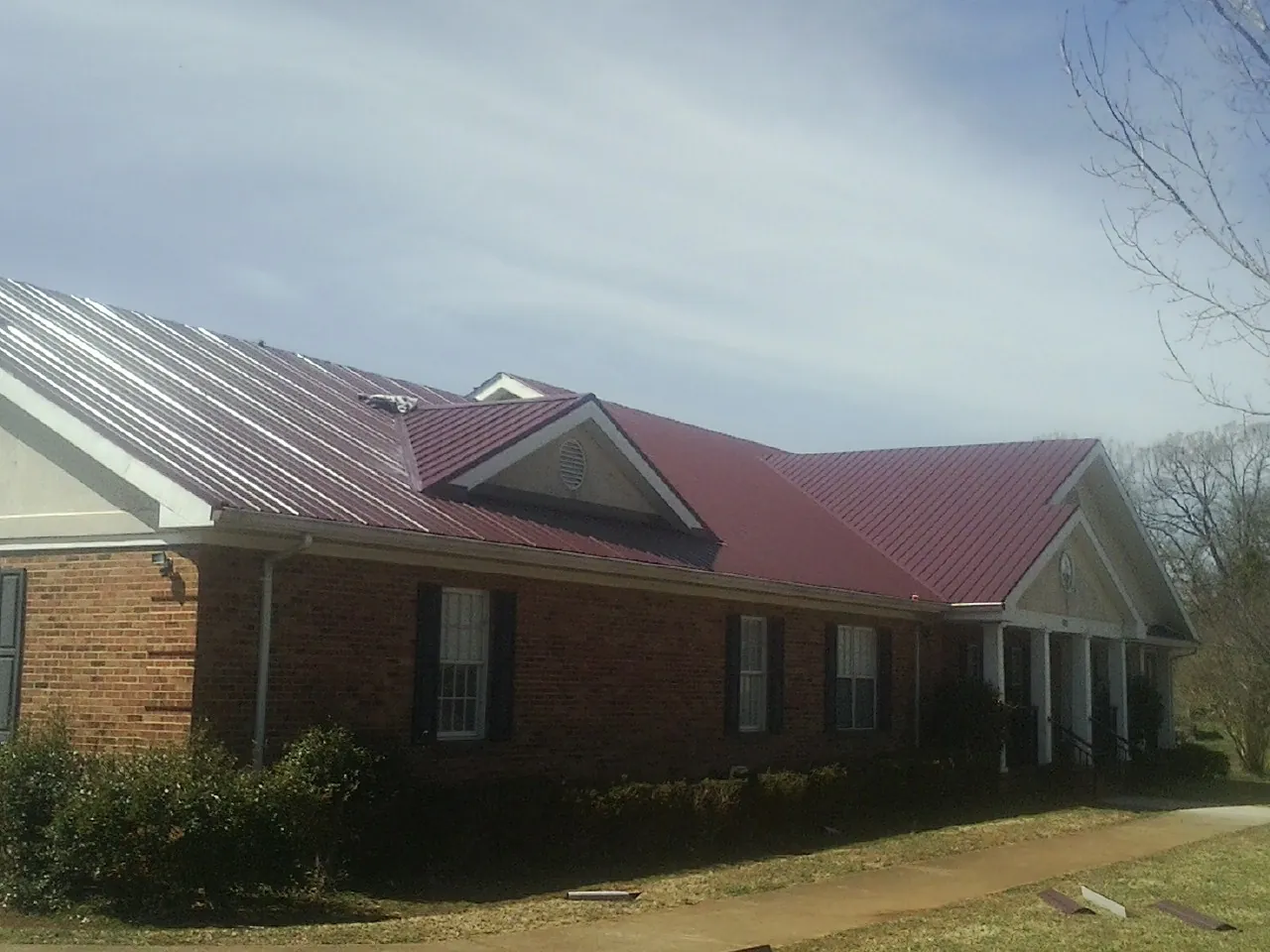 Red metal roof with gabled entries on a long brick building, from a Hail Damage Roof Repair job in Trumansburg