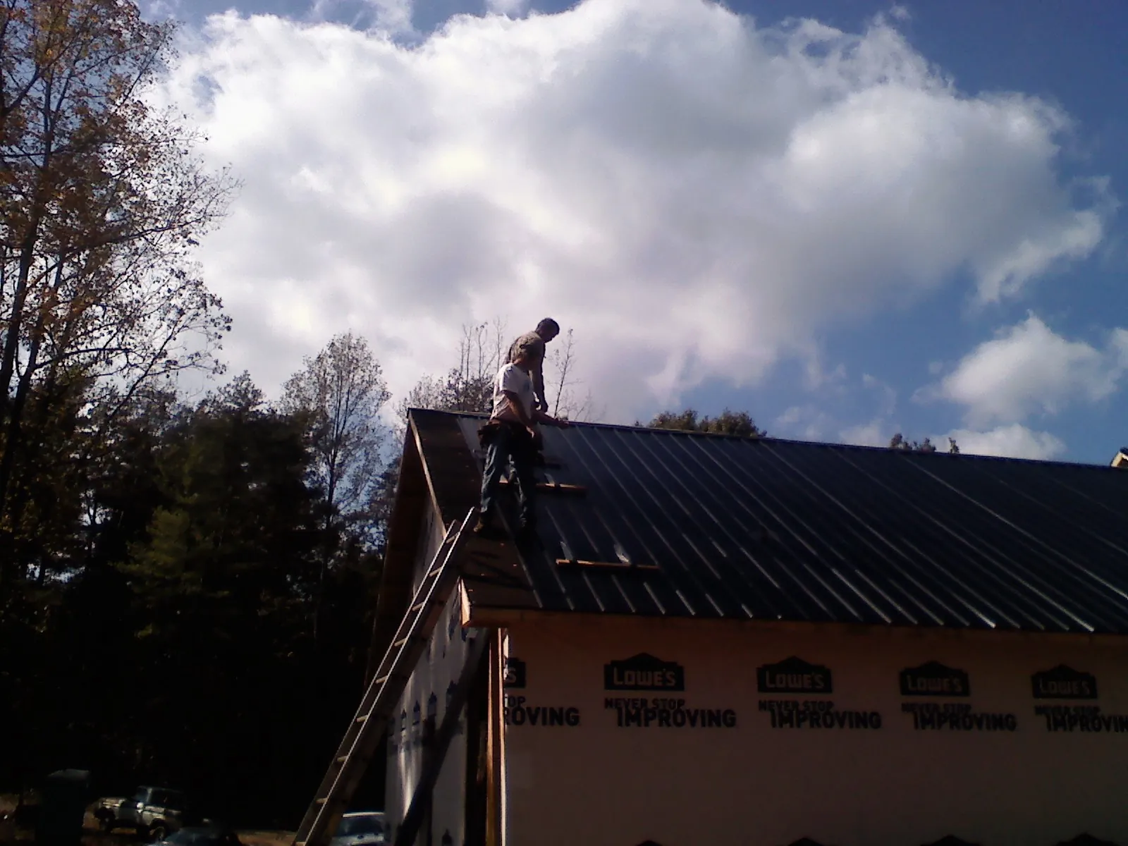 Roofer fastening dark metal panels high against a cloudy sky, from a Roof Inspection job in Trumansburg