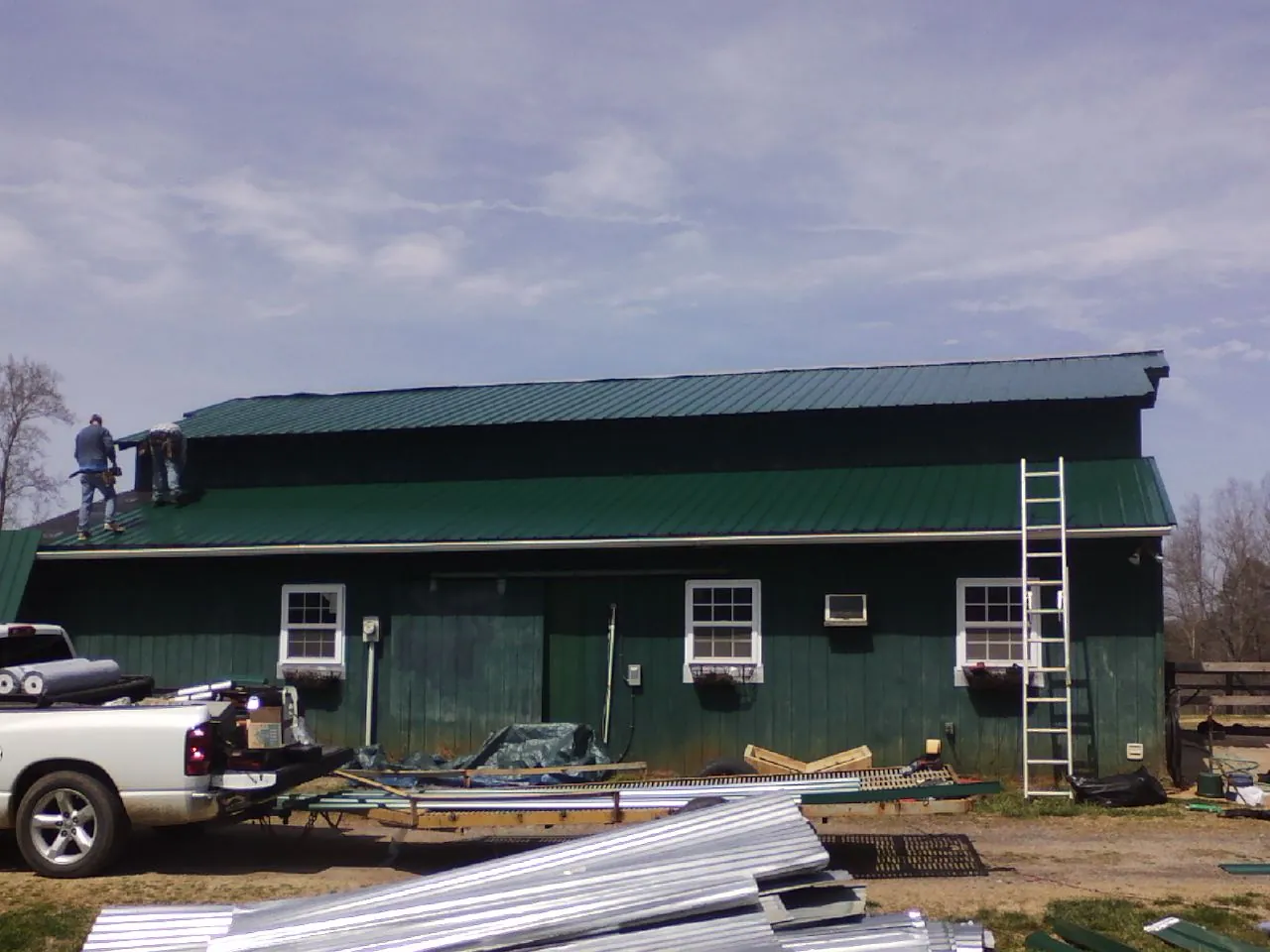 Crew installing green metal roofing on a large green barn in Trumansburg