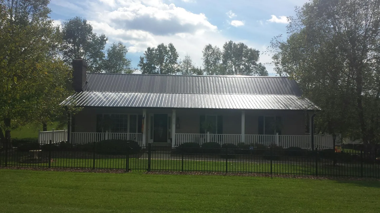 Gray metal roof on a brick ranch with a full width front porch — Gutter Guard Installation work by our crew in Trumansburg