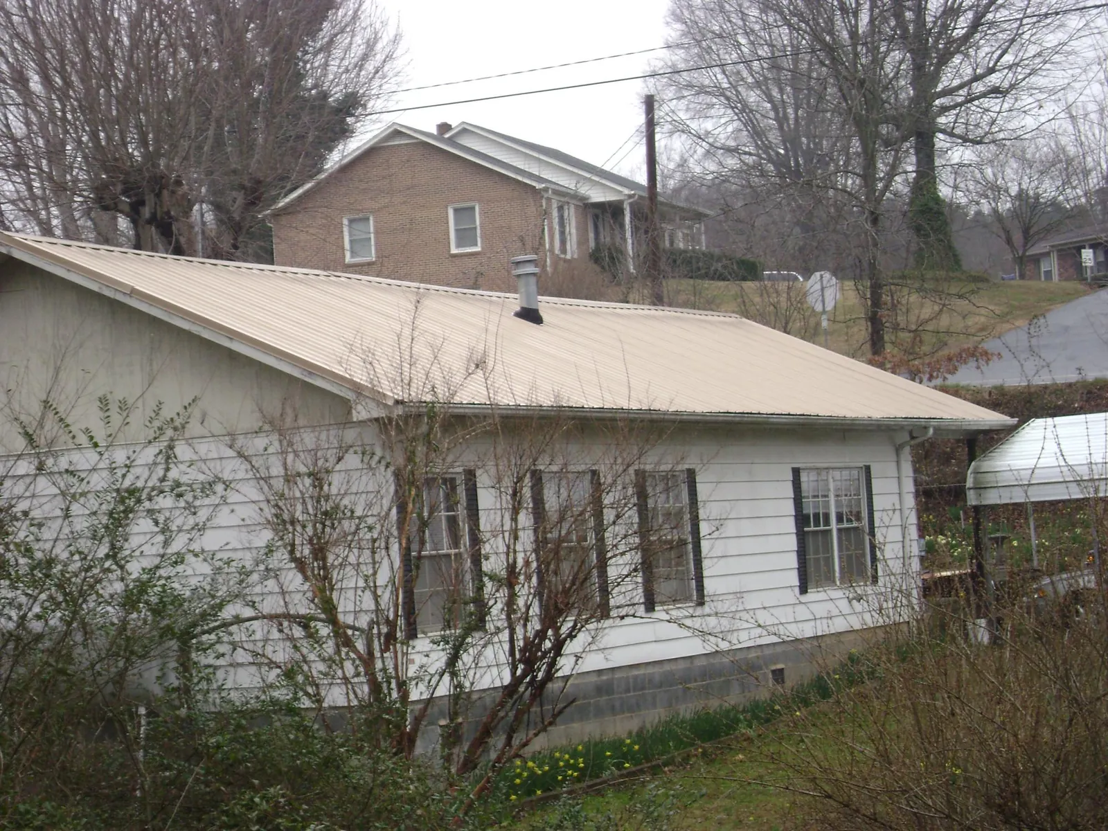 Tan metal roof on a white sided house set into a hillside — Commercial Roofing by Roofing Brothers in Trumansburg