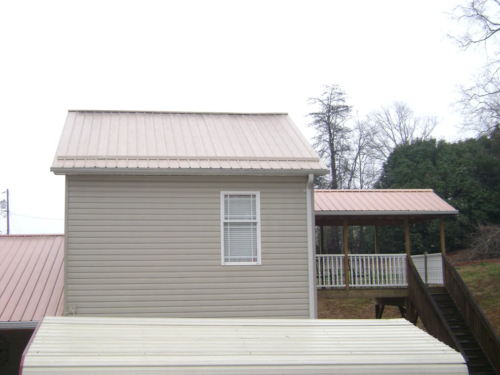 Tan metal roofs on a two story addition and attached porch, from a Roof Replacement job in Trumansburg