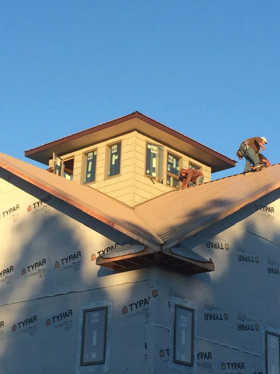 Roofers working around a rooftop cupola on a new metal roof at sunset — Roof Waterproofing in Trumansburg by Roofing Brothers